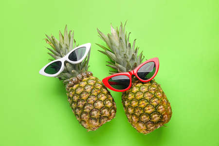 Pineapples with sunglasses on color background