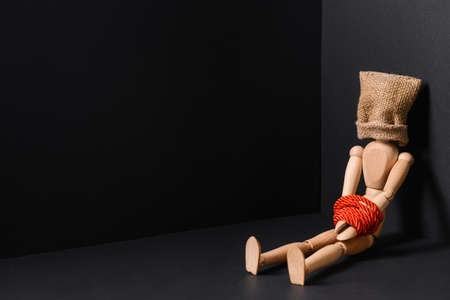 Mannequin with sack on head and hands tied with rope on dark background. Concept of hostageの写真素材