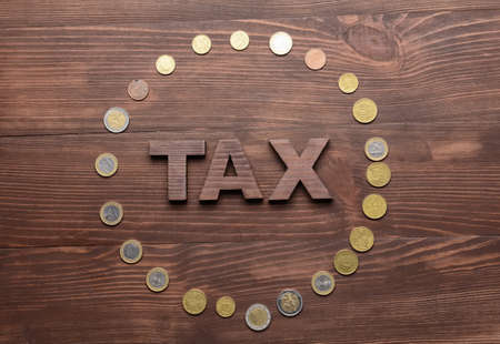 Word TAX with coins on wooden background