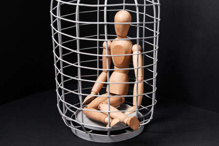 Mannequin sitting in cage on dark background. Concept of hostageの写真素材