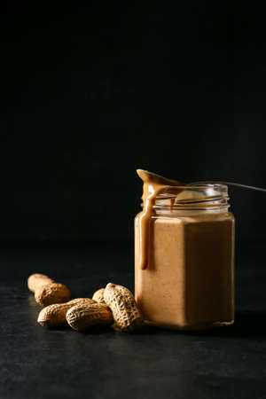 Jar with tasty peanut butter on dark background