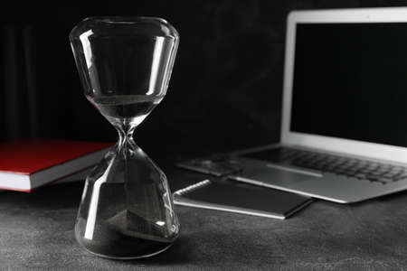 Stylish hourglass and laptop on dark table in office. Deadline conceptの写真素材