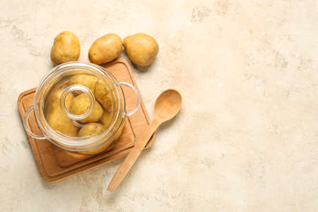 Cooking pot with raw potatoes and spoon on light backgroundの写真素材