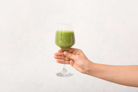 Hand with healthy vegetable smoothie on light background