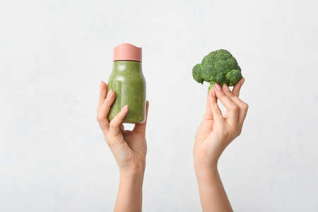 Hands with healthy vegetable smoothie and broccoli on light backgroundの写真素材
