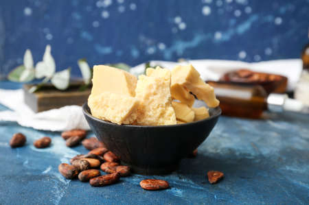 Bowl with cocoa butter and beans on color background, closeup