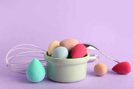 Baking dish with makeup sponges, spoon and whisk on color backgroundの写真素材