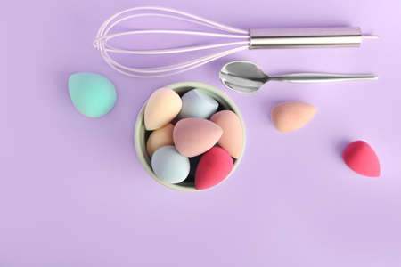 Baking dish with makeup sponges, spoon and whisk on color backgroundの写真素材