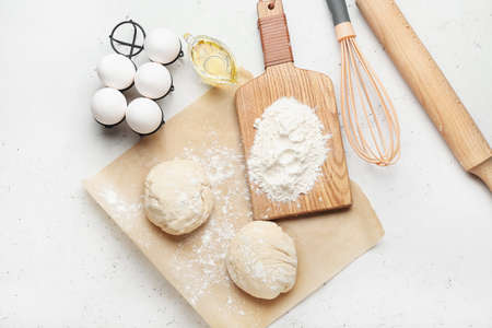 Fresh dough with ingredients for preparing bakery and utensils on light background