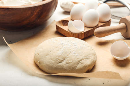 Fresh dough with ingredients for preparing bakery and utensils on light background
