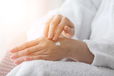 Young woman applying cosmetic cream onto her hands at home, closeupの写真素材