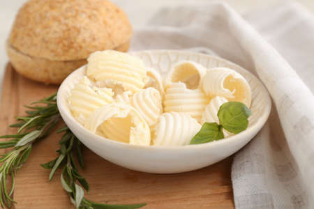 Bowl with fresh butter, bread, basil and rosemary on wooden boardの写真素材