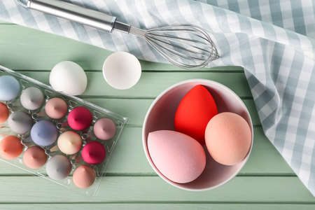 Creative composition with makeup sponges and whisk on color wooden background