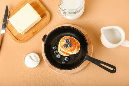 Frying pan with tasty cottage cheese pancakes and blueberry on color backgroundの写真素材
