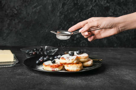 Woman sprinkling powdered sugar onto tasty cottage cheese pancakes on plate