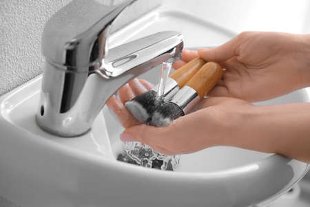 Woman washing makeup brushes under water