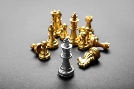 Silver king among golden chess pieces on gray background