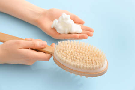 Female hands with massage brush and foam on color background, closeup