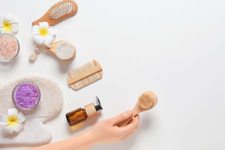Female hand with massage brush and bath supplies on white background