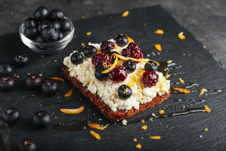 Tasty sandwich with cottage cheese, blueberries and blackberries on dark background
