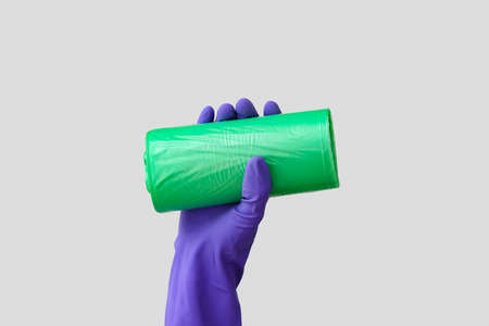Hand in rubber glove with roll of garbage bag on light backgroundの写真素材