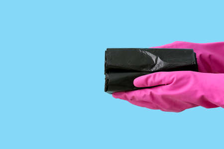 Hands in rubber gloves with rolls of garbage bags on color backgroundの写真素材