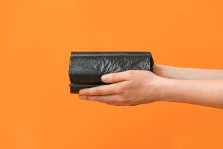 Woman holding rolls of garbage bags on color background