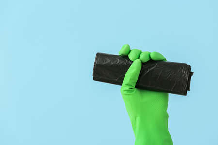 Hand in rubber glove with roll of garbage bag on color backgroundの写真素材