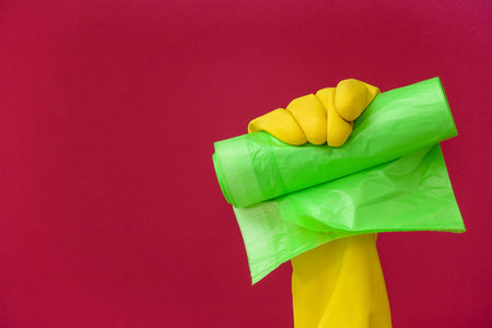 Hand in rubber glove with roll of garbage bag on color backgroundの写真素材