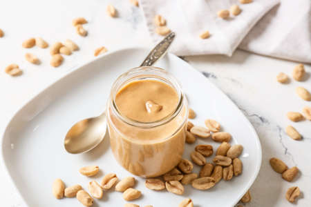 Jar with tasty peanut butter on light background