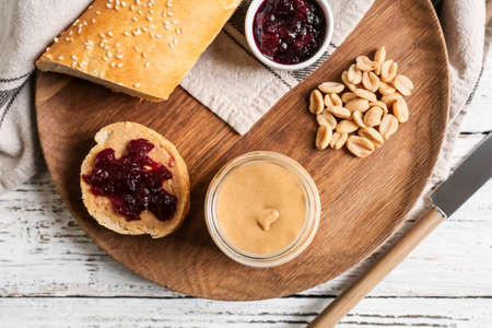 Jar with tasty peanut butter, bread and jam on light wooden backgroundの写真素材