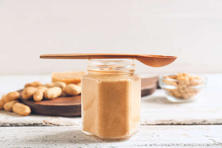 Jar with tasty peanut butter, bread and nuts on light wooden backgroundの写真素材