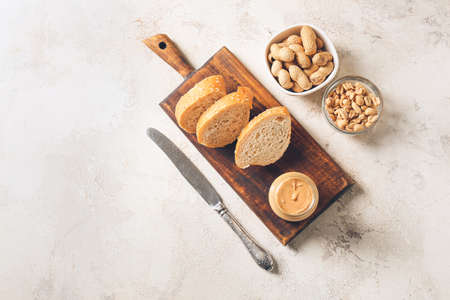 Jar with tasty peanut butter and pieces of bread on light backgroundの写真素材