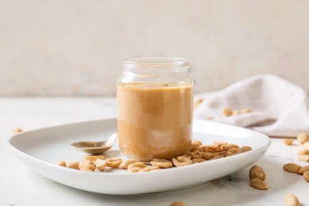 Jar with tasty peanut butter on light background