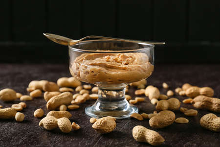 Glass bowl with tasty peanut butter and spoon on dark backgroundの写真素材