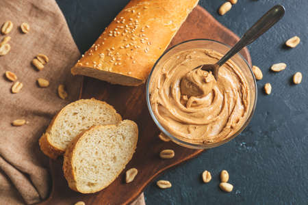 Glass bowl with tasty peanut butter and bread on dark backgroundの写真素材