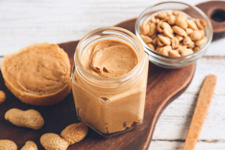 Jar with tasty peanut butter, bread and nuts on light wooden backgroundの写真素材