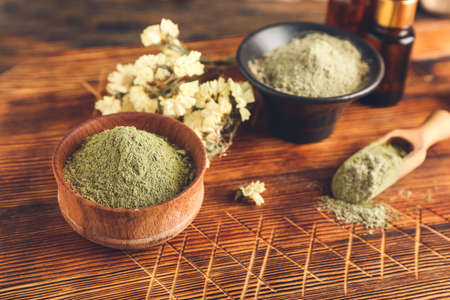 Dry henna powder in bowls and bottles of essential oil on wooden background, closeupの写真素材