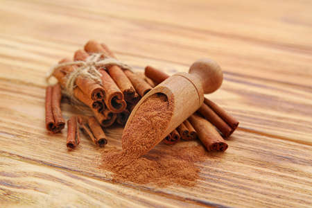Cinnamon sticks and scoop with powder on wooden background