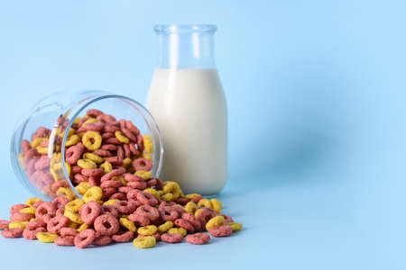 Glass with crunchy corn flakes rings and bottle of milk on color backgroundの写真素材