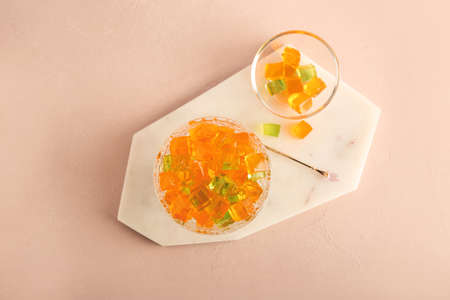 Glass bowl with tasty jelly cubes on color backgroundの写真素材