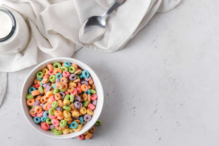 Bowl with crunchy corn flakes rings and milk on light background