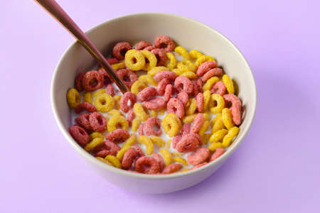 Bowl with crunchy corn flakes rings and milk on color background