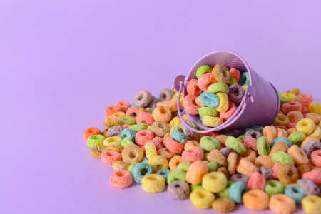 Small bucket with crunchy corn flakes rings on color background