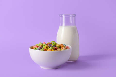 Bowl with crunchy corn flakes rings and bottle of milk on color backgroundの写真素材
