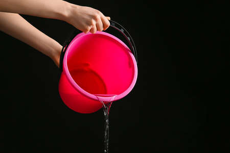 Woman pouring water from bucket on dark backgroundの写真素材