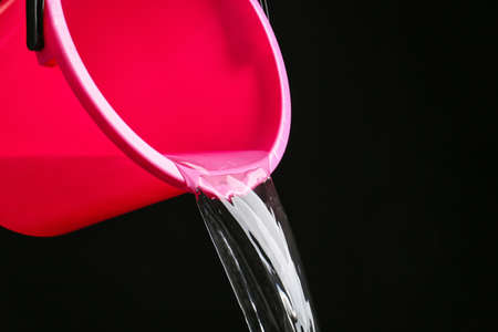 Pouring of water from bucket on dark background, closeupの写真素材