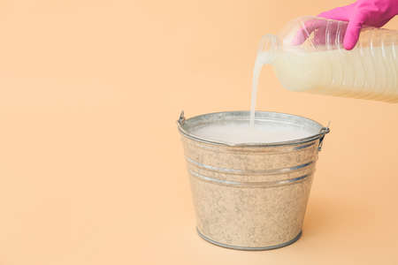 Woman pouring detergent into bucket on color backgroundの写真素材