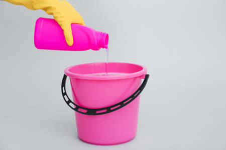 Woman pouring detergent into bucket on light backgroundの写真素材