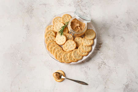Plate with tasty crackers and jar with peanut butter on light backgroundの写真素材